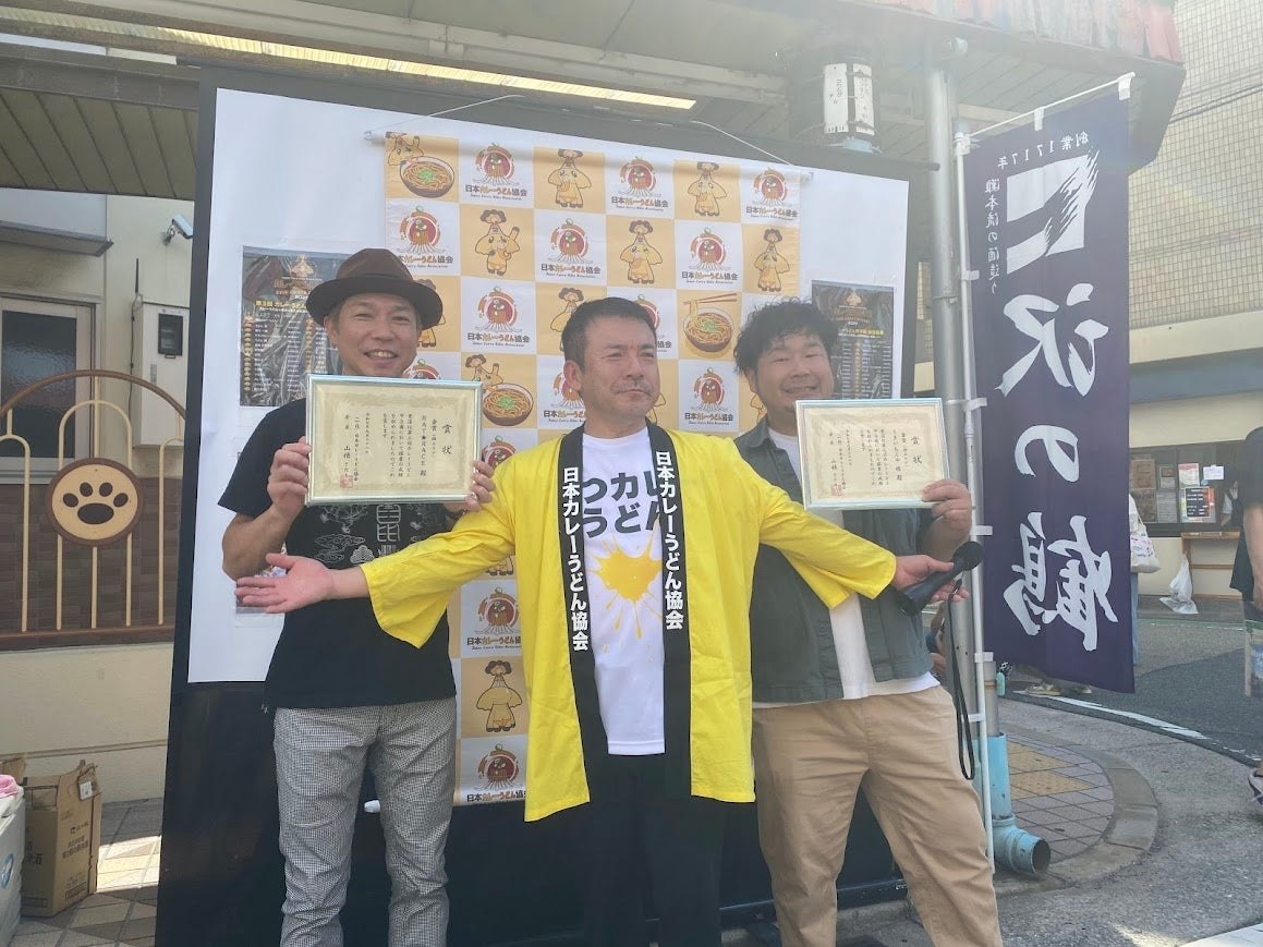 第3回カレーうどん甲子園の表彰式で賞状を持つ受賞店主と協会会長
