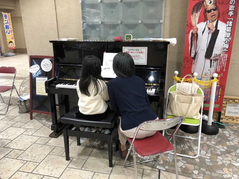 商店街のストリートピアノで講師とレッスンする女の子