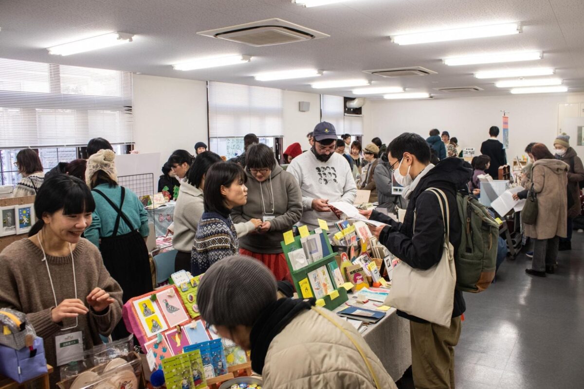 長机に並んだZINEや雑貨を手に取る来場者と出展者