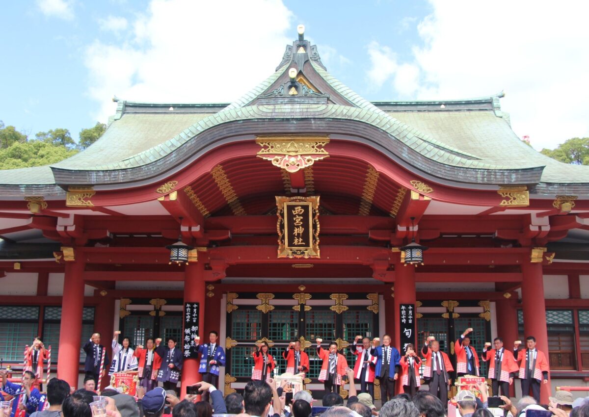 西宮神社の拝殿前で記念枡を掲げる一斉乾杯の様子