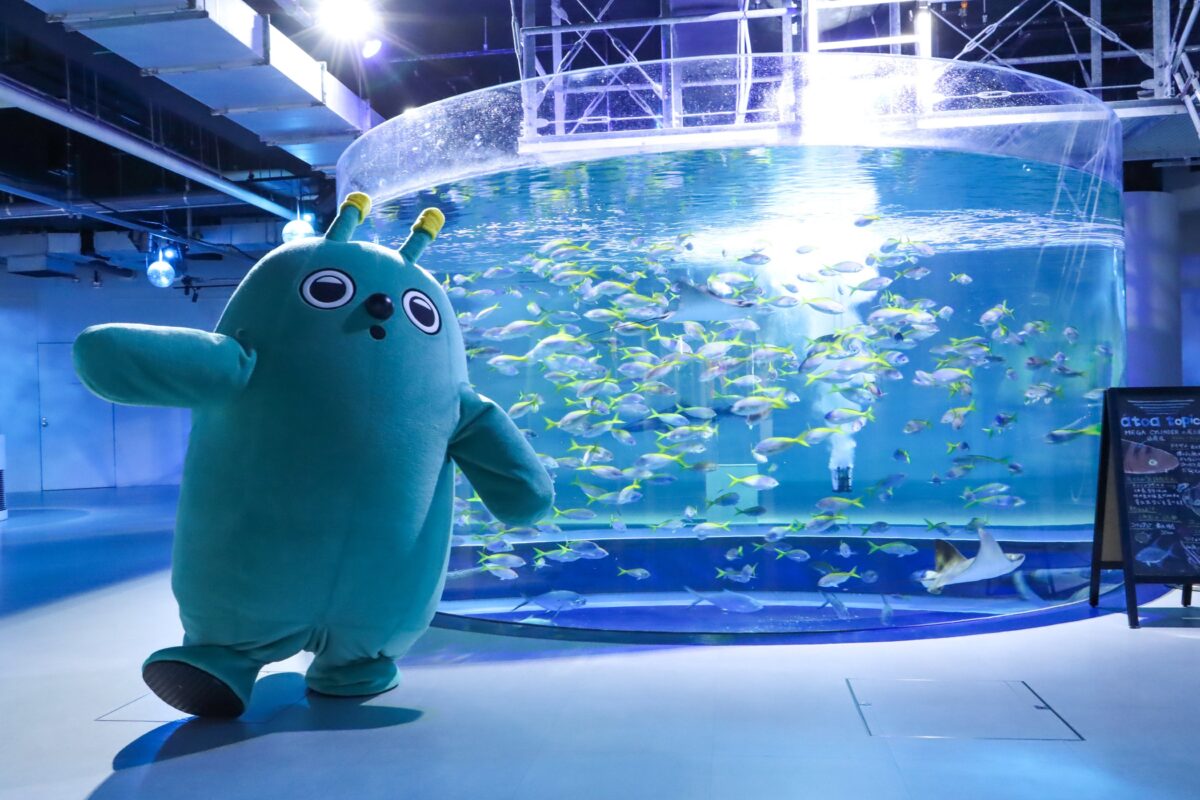 大水槽の前を歩くマスコットキャラクターのスピ