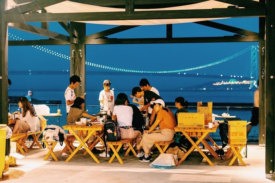 明石海峡大橋を望む夕暮れのBBQサイトで食事を楽しむ人たち